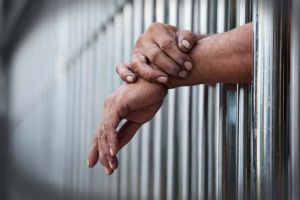 Person with hands out from jail bars