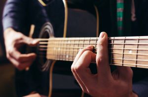 Man playing music at black wooden acoustic guitar. Focus on fingers.