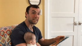Screen Shot of video. Luck reading a story with baby girl on his lap.