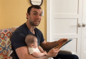 Screen Shot of video. Luck reading a story with baby girl on his lap.