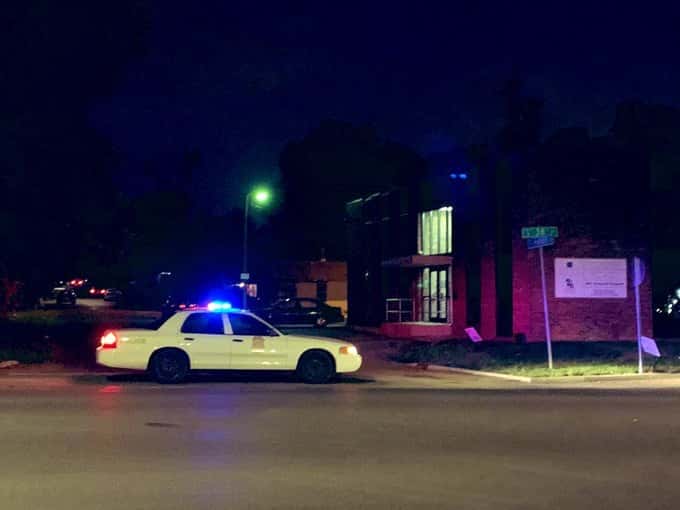 Police car parked in front of building on the east side at night with lights on.