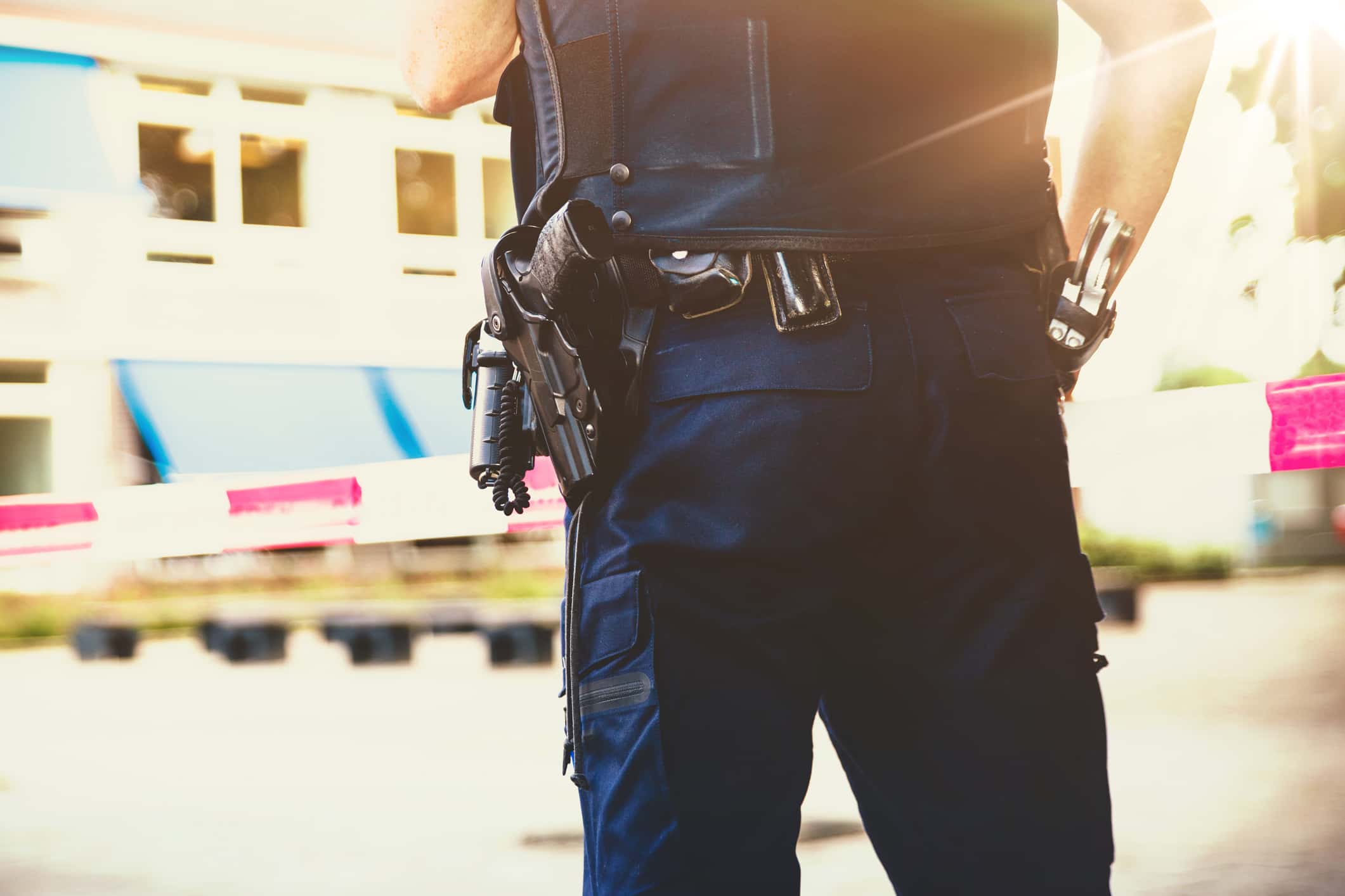 Policeman on crime scene . Red plastic tape and police officer, gun belt, handcuffs and gun.With a sunshine flare coming in.