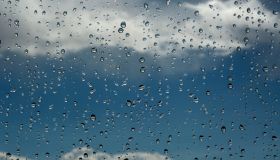 Rain drops cover the image, containing clouds and a dim, blue sky in the background.