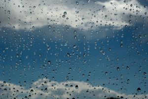 Rain drops cover the image, containing clouds and a dim, blue sky in the background.