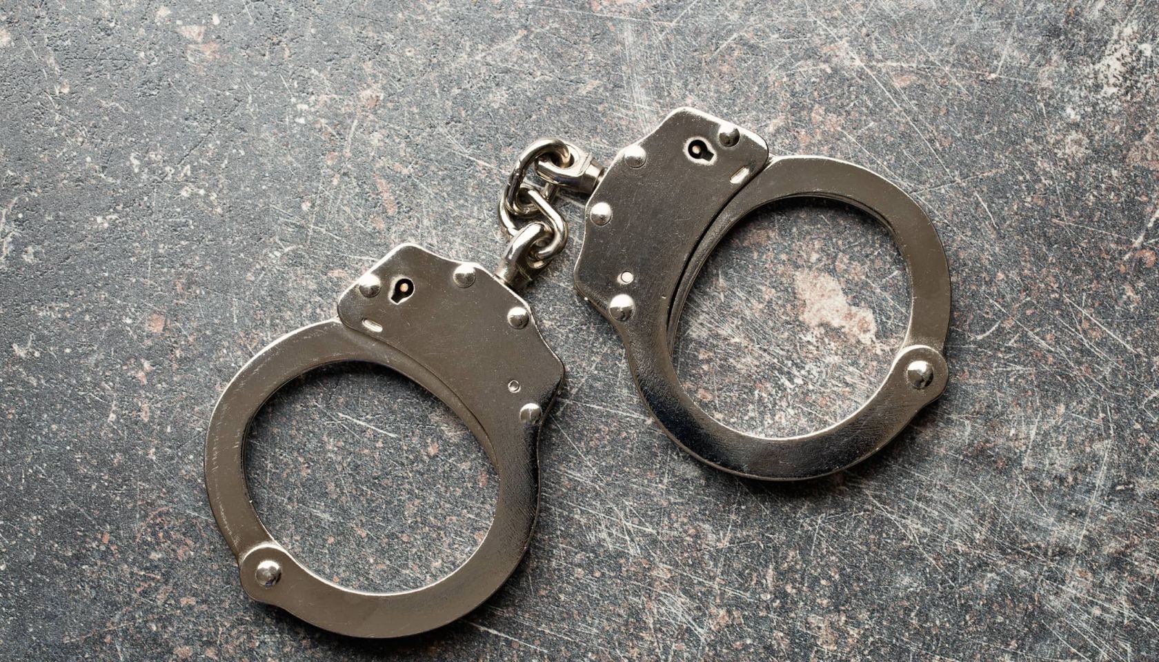 Silver handcuffs on a crackled gray background.