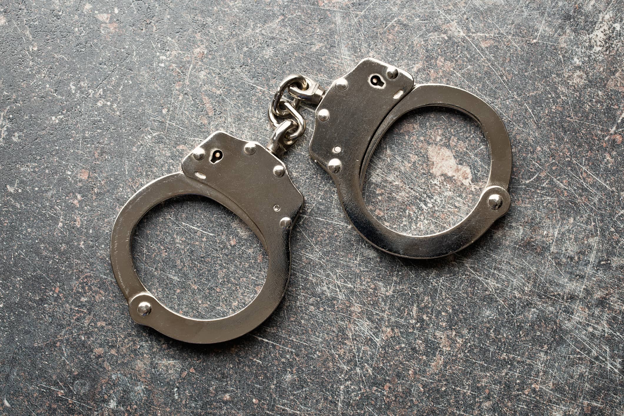 Silver handcuffs on a crackled gray background.