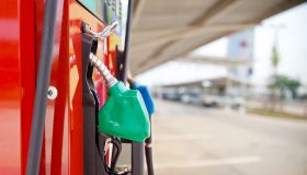 A car filling up with gasoline at a gas station showing a close up of the pump in the gas tank from a side view.