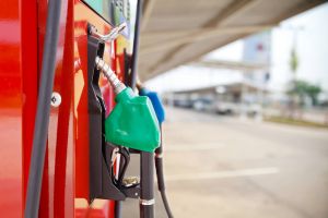 A car filling up with gasoline at a gas station showing a close up of the pump in the gas tank from a side view.