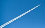 An airplane flies through a bright, blue sky