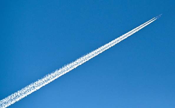An airplane flies through a bright, blue sky
