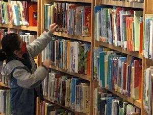 A young girl reaches to pull a book off the shelves at the Indianapolis Public Library.