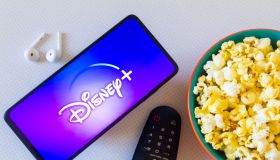 In this photo illustration, the Disney+ (Plus) logo seen displayed on a smartphone along with a bowl of popcorn, headphones, and a tv remote. (Photo Illustration by Rafael Henrique/SOPA Images/LightRocket via Getty Images)