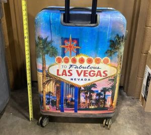 A hard shell suitcase, with Las Vegas written against a blue background and rollers on the bottom.