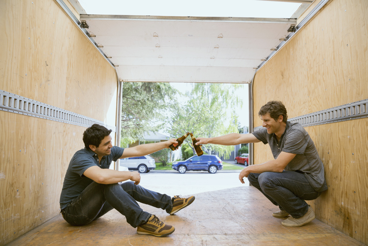 Men toasting beer bottles inside moving van