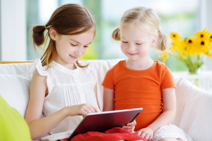 Two adorable little sisters playing with a digital tablet