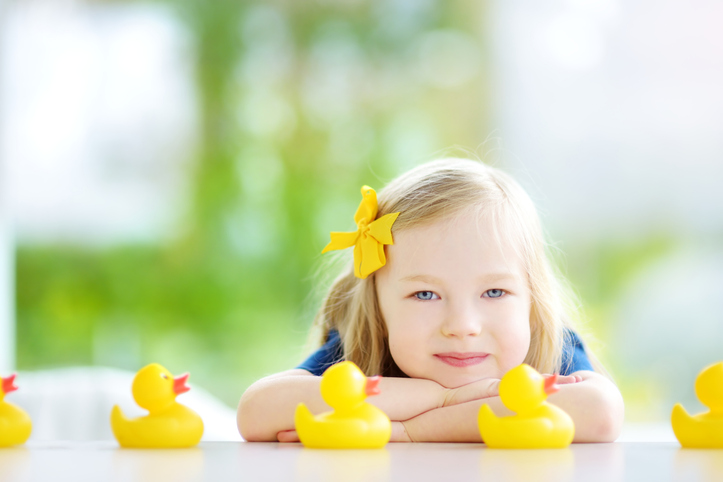 Cute little girl playing with rubber ducklings at home
