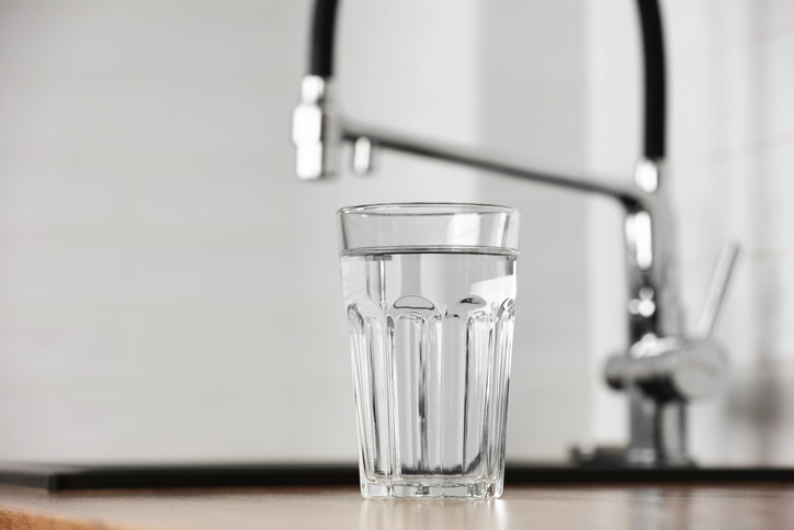 Transparent glass of clean filtering water on wooden table in kitchen interior. Tap with purified water with an osmosis system of the home kitchen sink