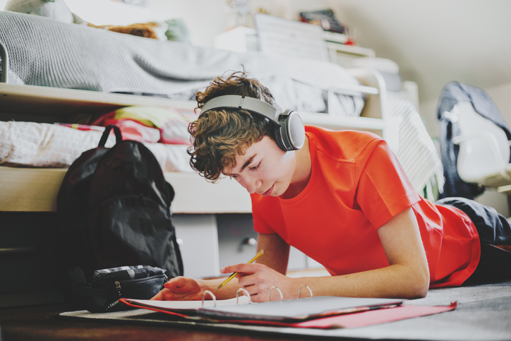 teenager studying and doing home works on the carpet wearing headphones