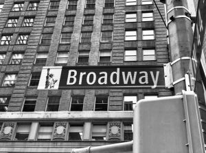 Grayscale low-angle shot of a street sign with a direction to Broadway in New York