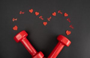 Gym dumbbells and red decorations in shape of a heart for Valentine's Day.