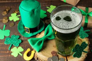 St.Patrick 's Day. celebration. green beer, leprechaun hat, coins, bow tie and clover on a brown background.
