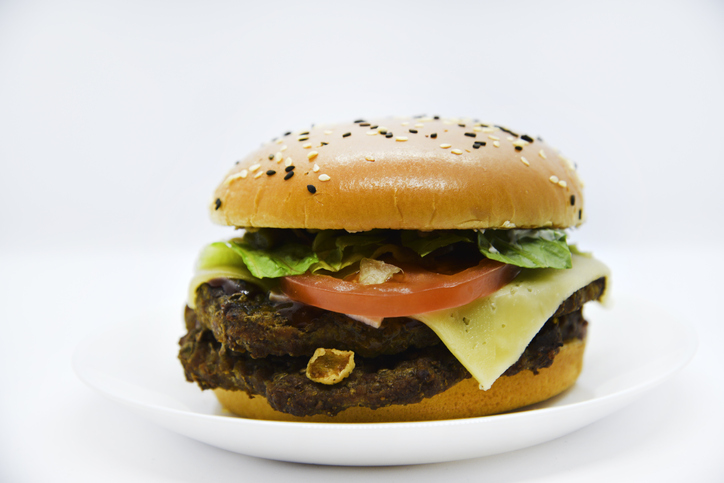 Double meat burger with vegetables on a white background. Delicious cheeseburger on a plate. Meat fast food. A large hamburger with a double cutlet.