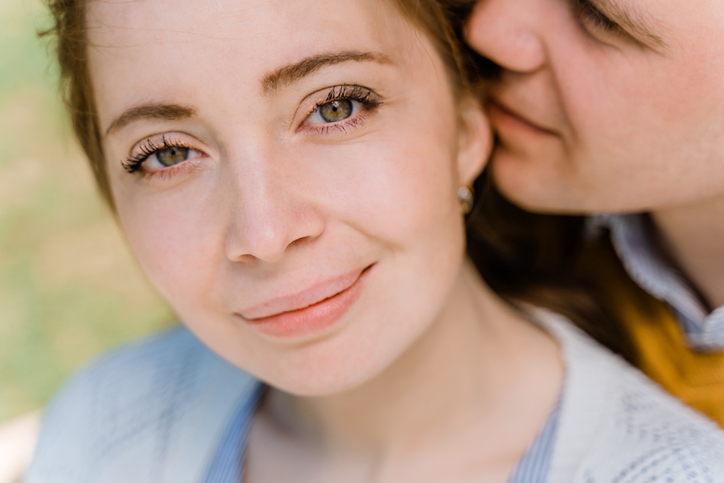close-up of a man and woman gently hugging and kissing, woman looks and smile