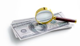 One hundred US dollar banknotes and a gold magnifying glass against a white background