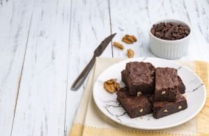 Brownies on a plate with chocolate pieces and walnuts over white wooden table with copy space