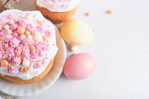 Traditional Easter sweet bread or cakes with white icing and sugar decor, colored eggs and cherry blossom tree branch over white table. Various Spring Easter cakes. Happy Easter day. Selective focus.