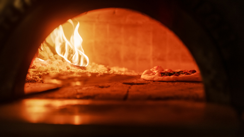 In Restaurant Pizza Peel Transferring Pizza into Wood Fire Stone Oven. Traditional Cooking, Italian Family Recipe. Authentic Pizzeria with Delicious Organic Food. Cinematic No People Shot