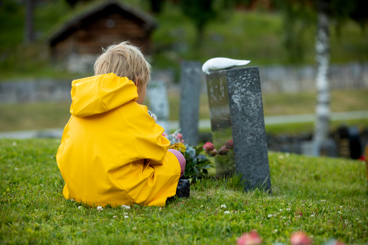 Sad little child, blond boy, standing in rain on cemetery, sad person, mourning