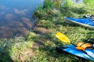 Tourist canoes with paddles stand on the river coast in summer on a water hike. Rafting on inflatable and frame double and triple kayak boats, family trip, extreme adventure in summer