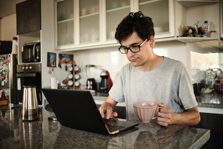 adult man works on his laptop from home holds cup of coffee