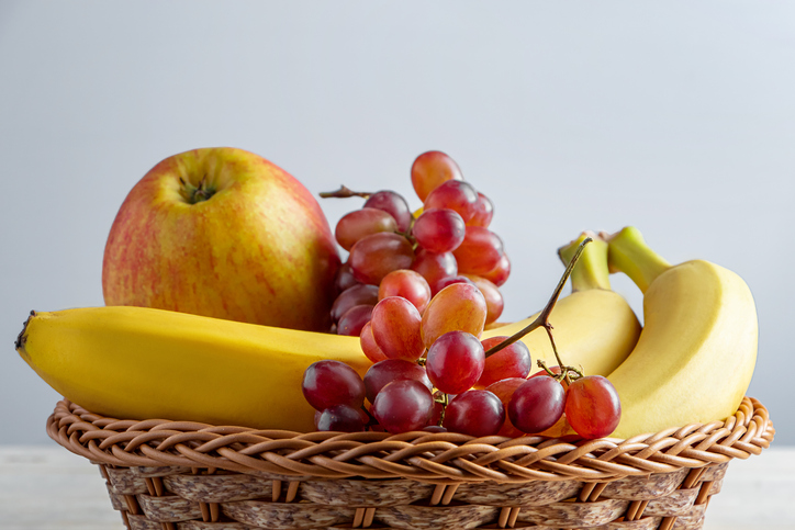Ripe fruits in wicker basket on gray background Harvest concept Bananas,Apples and grapes,Romania