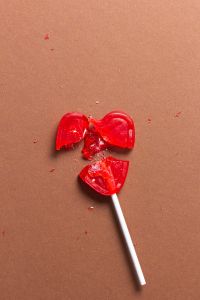 Red heart shaped lollipop broken into several pieces on a brown background.