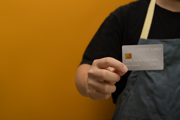 Man small business owner wearing apron holding credit card. Electronic money, contactless payment concept.