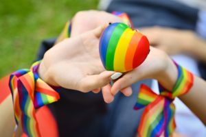 Closeup view of LGBT friends holding rainbow heart, celebrating gay pride, enjoying outdoor activities outdoor. LGBT community concept.