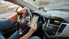 Hands of unrecognizable man driver using white screen mockup mobile phone while driving