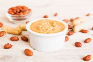 Bowl of peanut butter and peanuts on table background. top view with copy space. Creamy peanut pasta in small bowl