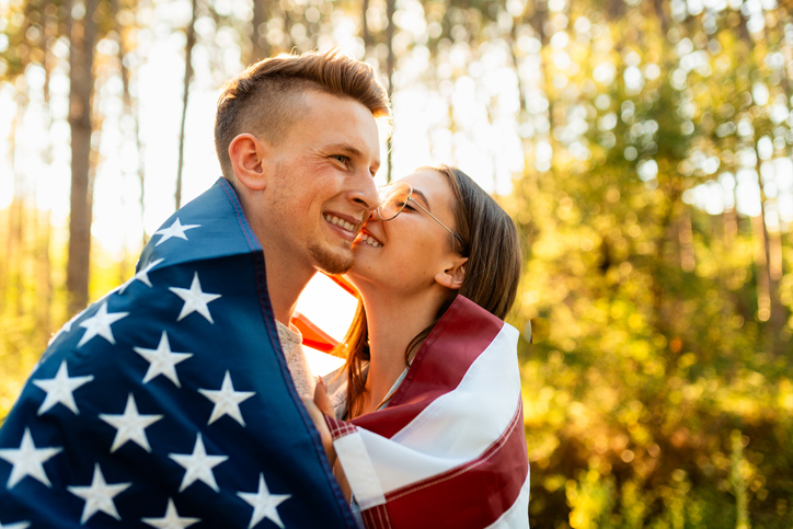 Young couple wrapped with American flag showing their love on Independence day
