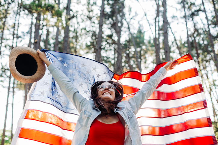 Young woman cheering and jumping with American flag outdoors