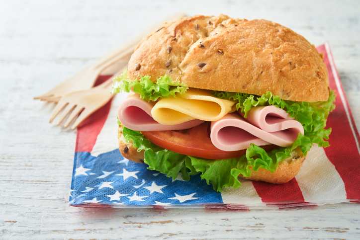 4th of July American Independence Day traditional picnic food. American sandwich or Burger on white, American flags and symbols of USA Patriotic picnic holiday on white wooden background. Top view