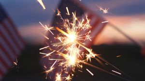 Fireworks sparklers fourth of July, Happy USA Independence Day Holiday, Celebration. Hands Holding Sparklers Fireworks with USA American Flag at sunset outdoor background. Concept 4th of July, Freedom