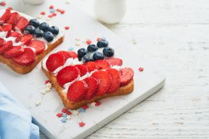 4th of July American Independence Day food. American flag sandwich with strawberries, blueberries, whipped sweet cream, soft cheese on toast bread. Independence or Patriotic Day breakfast idea Mock up
