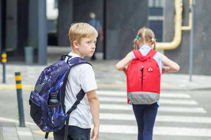 Back to school. Little pedestrians with backpacks walk to school and cross road at crosswalk.