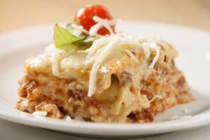 homemade lasagna portion on white plate on wood table