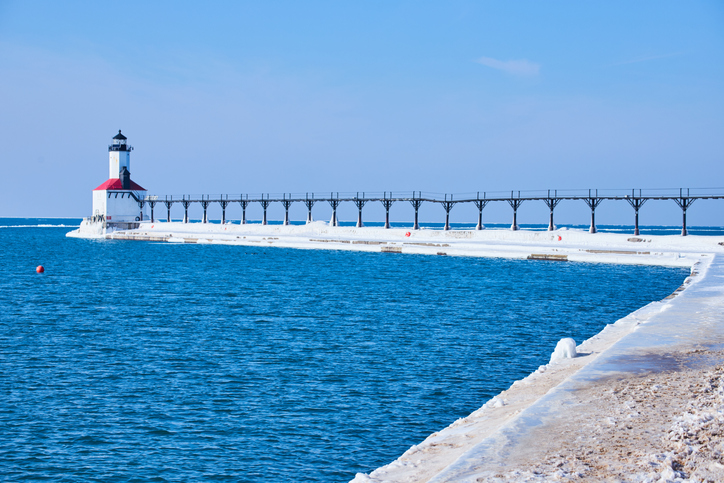 White and red lighthouse on lake in winter with snow