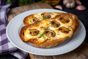 Toasted sandwich from traditional sourdough bread with cheese and brown mushrooms seasoned with rosemary herb on a wooden board, top view