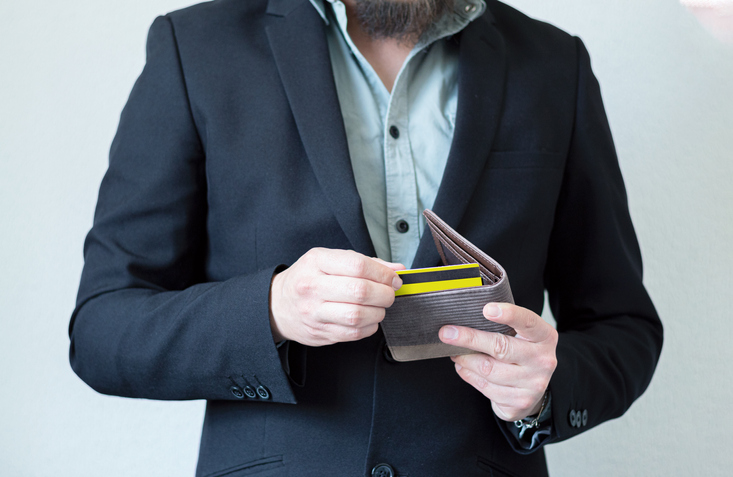 Unrecognizable businessman in a suit taking out a yellow credit card from a stylish wallet. Plastic money concept